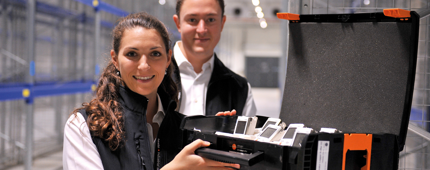 Mitarbeiter von Testo Industrial Services stehen mit einem Koffer voller Datenlogger in einem Hochregallager und bereiten ein Mapping vor.